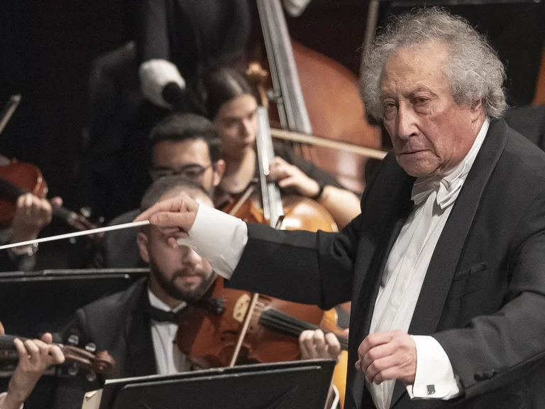 Ein Dirigent leitet ein klassisches Orchester, Musiker spielen Streicher. Der Dirigent trägt einen schwarzen Frack und einen weißen Frackhemd.