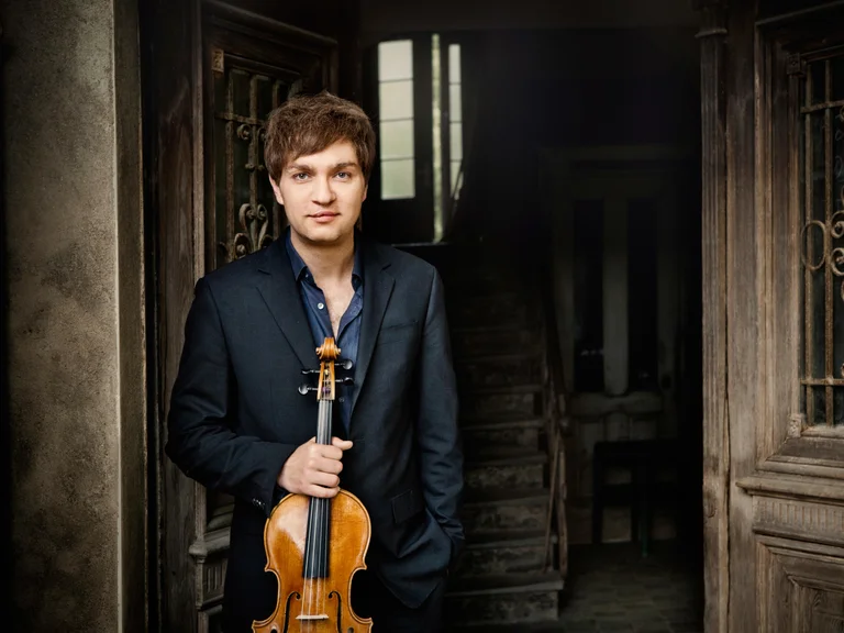 Nils Mönkemeyer: Ein Mann in einem Anzug steht in einem dunklen Raum und hält eine Geige. Im Hintergrund eine Treppe.