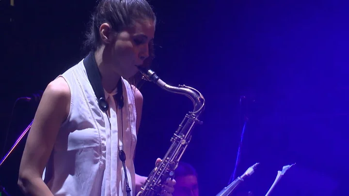 Melissa Aldana spielt Saxophon auf der Bühne. Blaues Licht beleuchtet die Szene.
