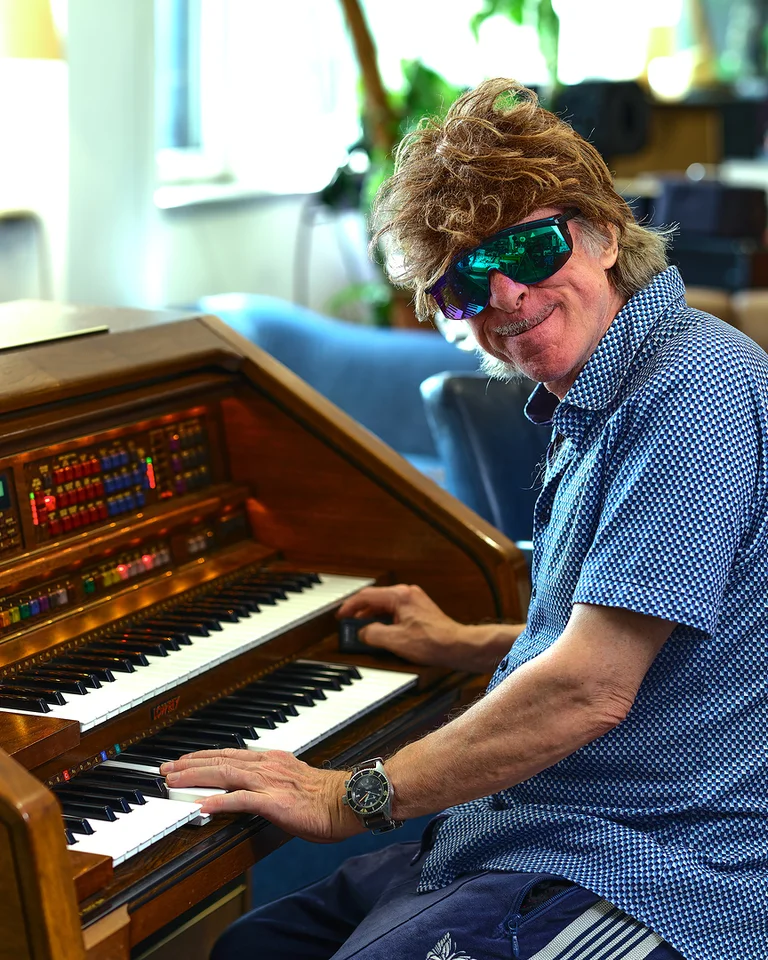 Eine Person (Helge Schneider) mit Sonnenbrille spielt an einem elektronischen Keyboard. Im Hintergrund sind gemütliche Möbel zu sehen.