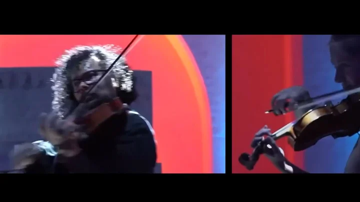 Two musicians from the Treppenhausorchester play the violin on a stage with a colorful background.