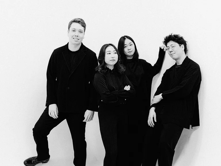 Eine Gruppe von vier Personen (Leonkoro Quartett) steht in schwarzer Kleidung vor einem weißen Hintergrund. Sie lächeln entspannt in die Kamera.