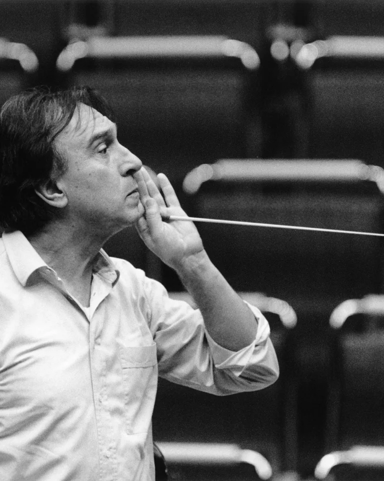 Ein Dirigent steht vor leeren Sitzen mit einem Taktstock in der Hand, konzentriert auf eine imaginäre Aufführung vor ihm.