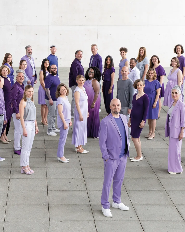 A large group of people dressed in various shades of purple and grey standing on a paved area.