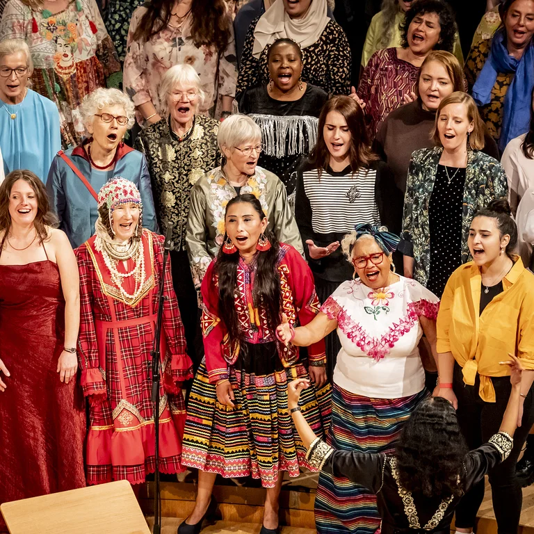 A group of people in colorful traditional clothing stands on a stage, apparently singing together.