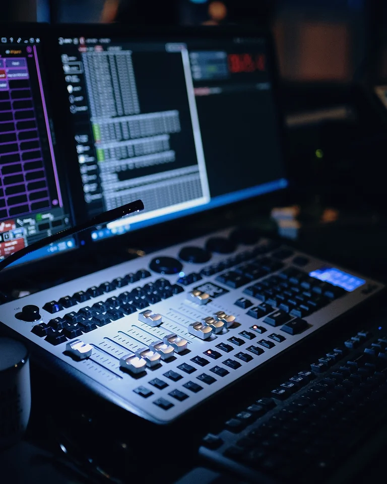 Ein Audio-Mischpult mit mehreren Bildschirmen in einem schwach beleuchteten Raum, ideal für Musikproduktion oder Live-Eventsteuerung.