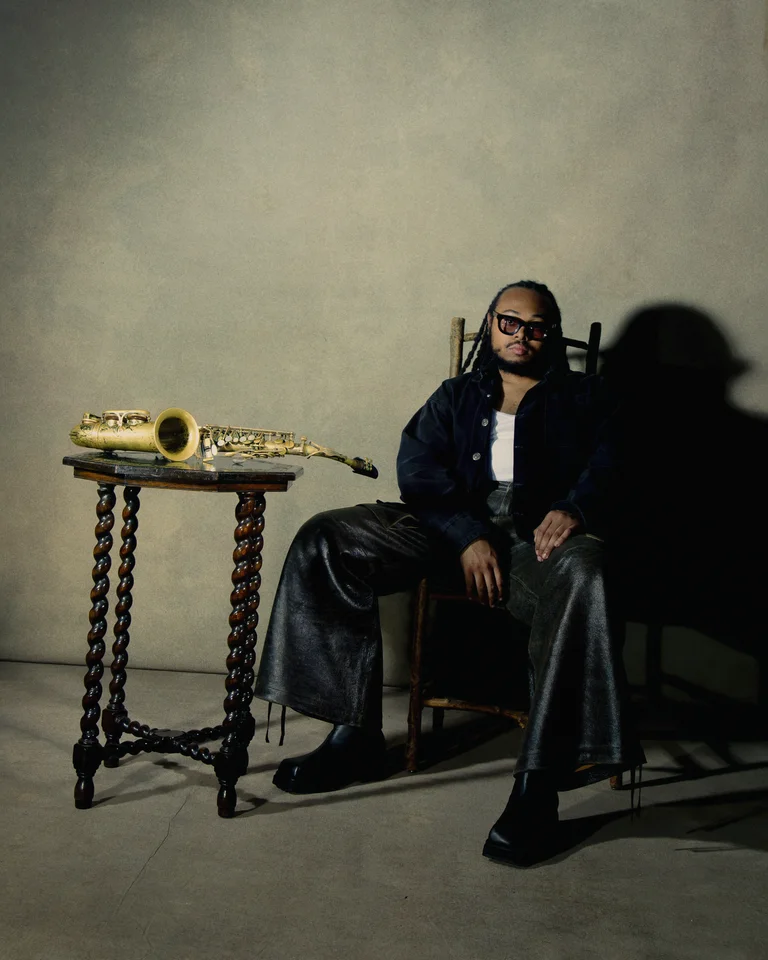 Eine Person (Immanuel Wilkins) sitzt entspannt auf einem Stuhl neben einem Tisch mit einem goldenen Saxophon.