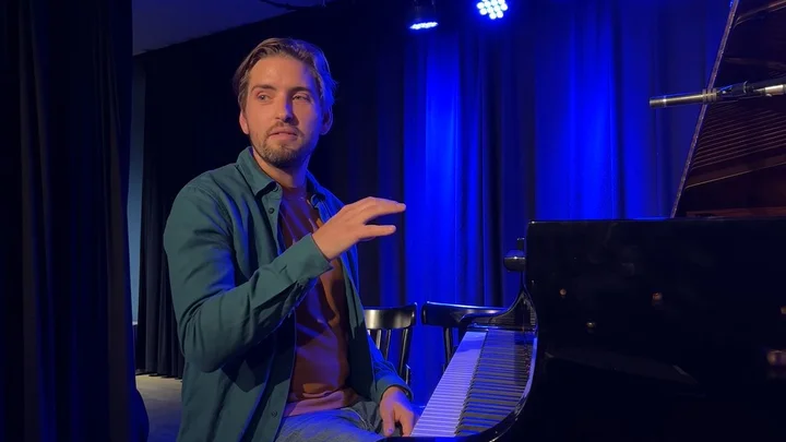 Pablo Held sits at a piano on a stage bathed in blue light and explains his music.