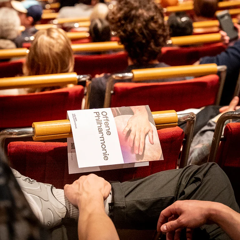 Ein Konzertsaal voller Menschen mit einem Programmheft »Offene Philharmonie« auf dem Schoß eines Zuschauers im Vordergrund.