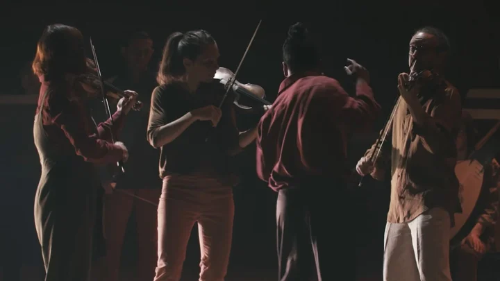 Members of Le Concert de la Loge play their violins on a dimly lit stage.