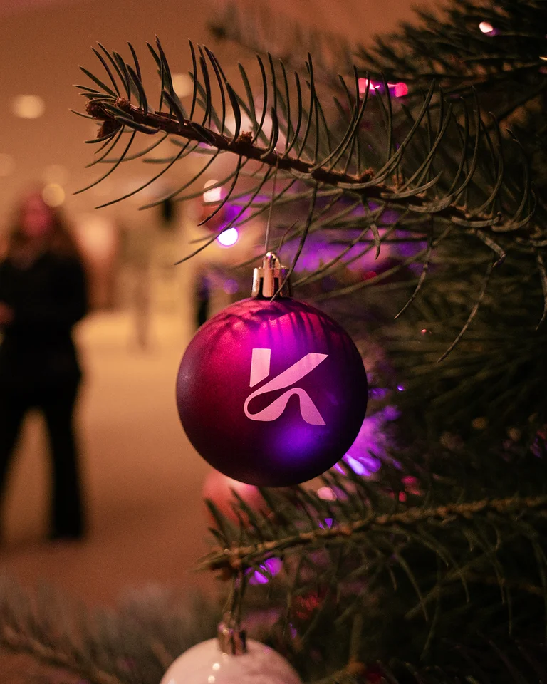 Ein Geschmückter Weihnachtsbaum im Foyer der Kölner Philharmonie mit lila Kugel im Vordergrund. Im Hintergrund sind unscharf Menschen und warme Beleuchtung zu sehen.