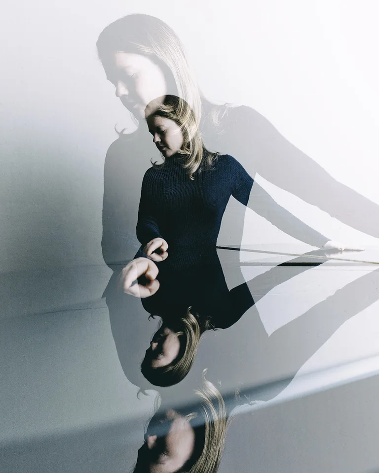 Eine Frau in einem dunklen Oberteil und ihre Spiegelung auf einer glänzenden Oberfläche, mit verschwommenem, künstlerischem Effekt.