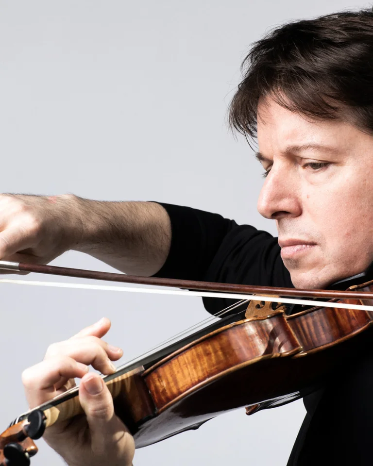 Ein Mann spielt konzentriert Violine. Er trägt ein dunkles Hemd und hält die Geige mit Präzision gegen einen neutralen Hintergrund.