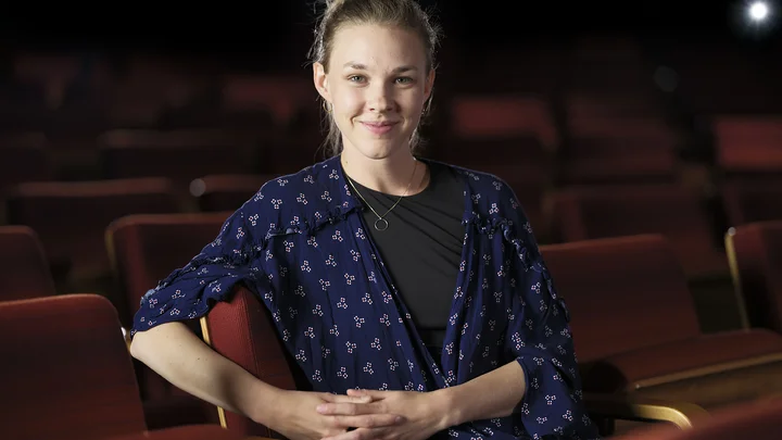 Valerie Fritz sitzt lächelnd auf einem Publikumsplatz im Saal der Kölner Philharmonie.