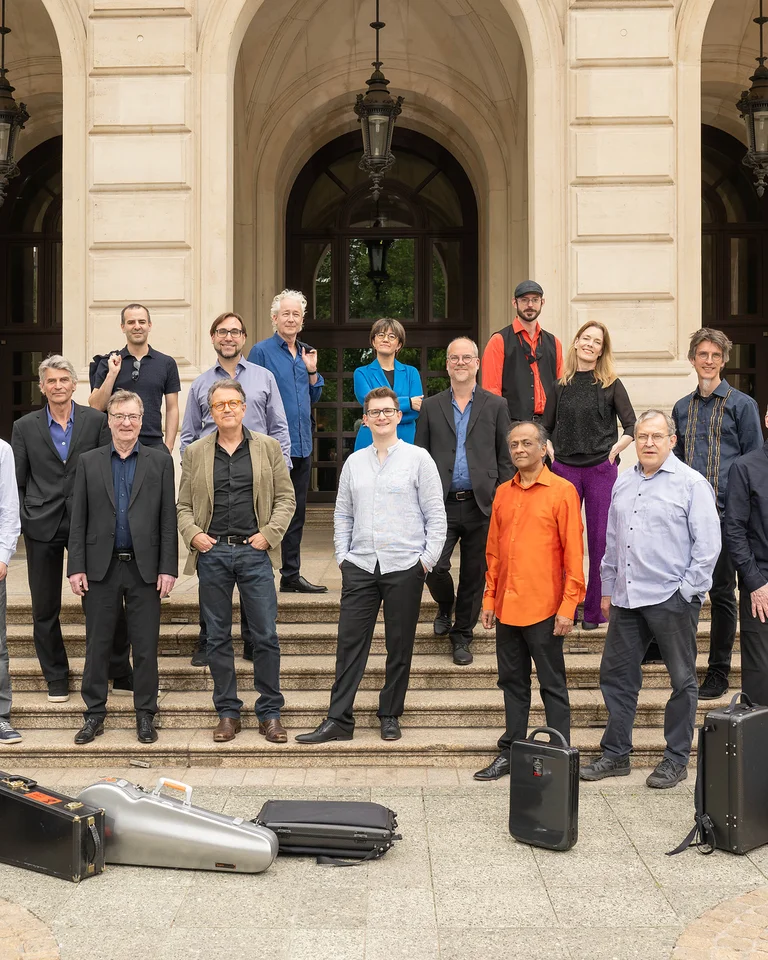 The Ensemble Modern stands in front of the Alte Oper Frankfurt, surrounded by musical instrument cases.