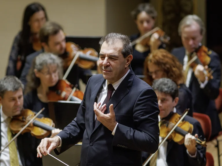 Daniele Gatti mit Sächsische Staatskapelle Dresden: Ein Dirigent leitet ein Orchester, während mehrere Musiker Streichinstrumente spielen. Die Atmosphäre ist konzentriert und musikalisch.