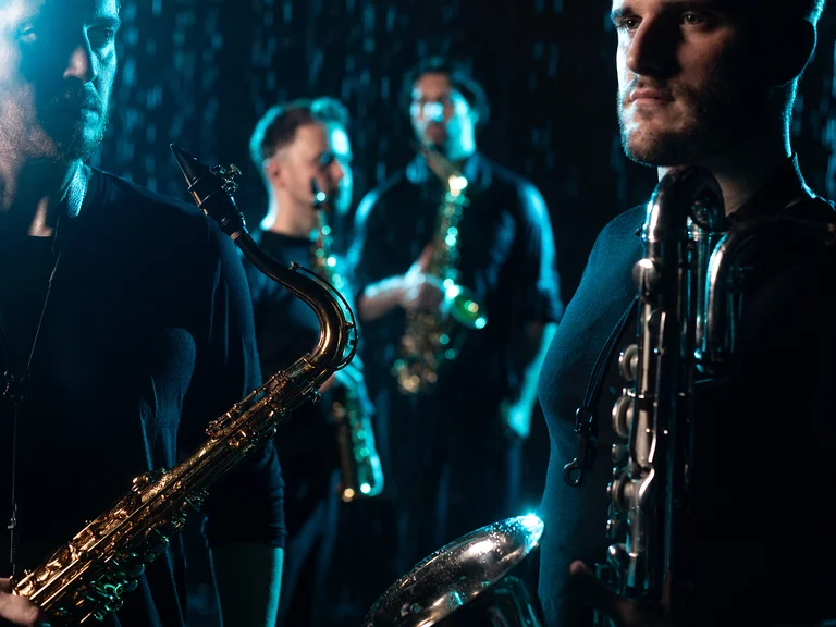 Vier Musiker (SIGNUM Quartett) spielen Saxophon in gedämpfter Beleuchtung, was eine stimmungsvolle und intime Atmosphäre schafft.