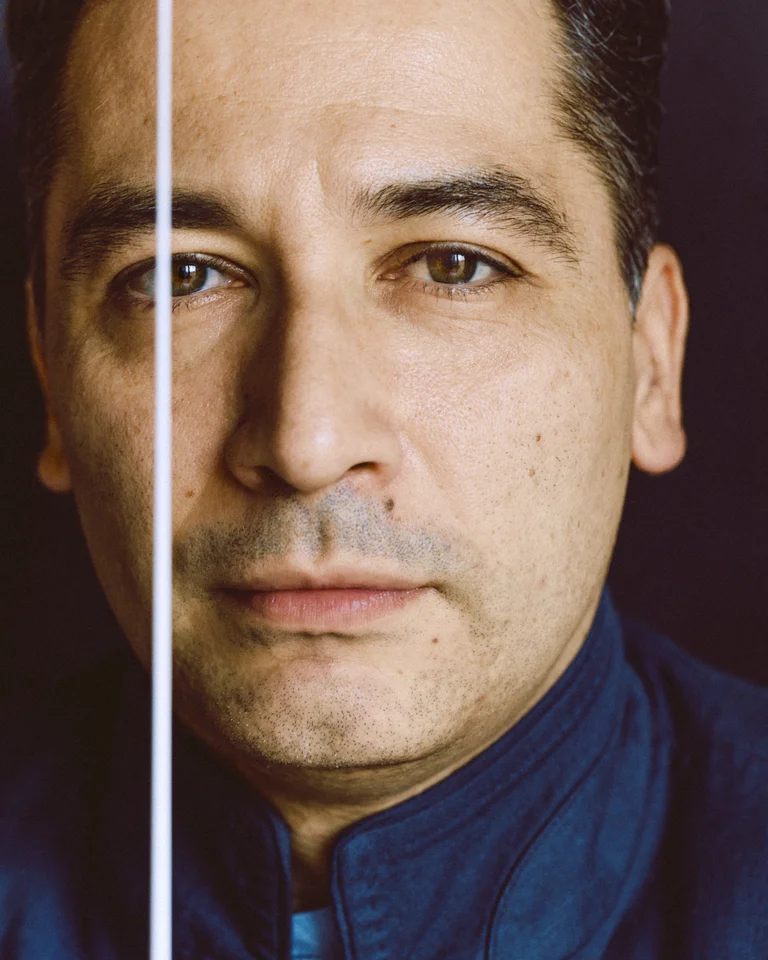 Ein Porträt eines Mannes in naher Aufnahme. Er trägt eine dunkle Jacke. Der Hintergrund ist dunkel gehalten.