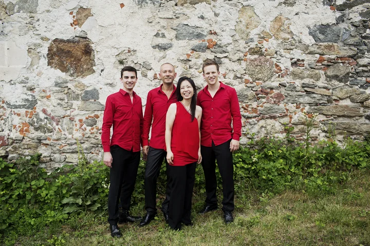 Die Mitglieder des Wave Quartet stehen vor einer alten Steinmauer. Sie tragen rote Oberteile und schwarze Hosen.