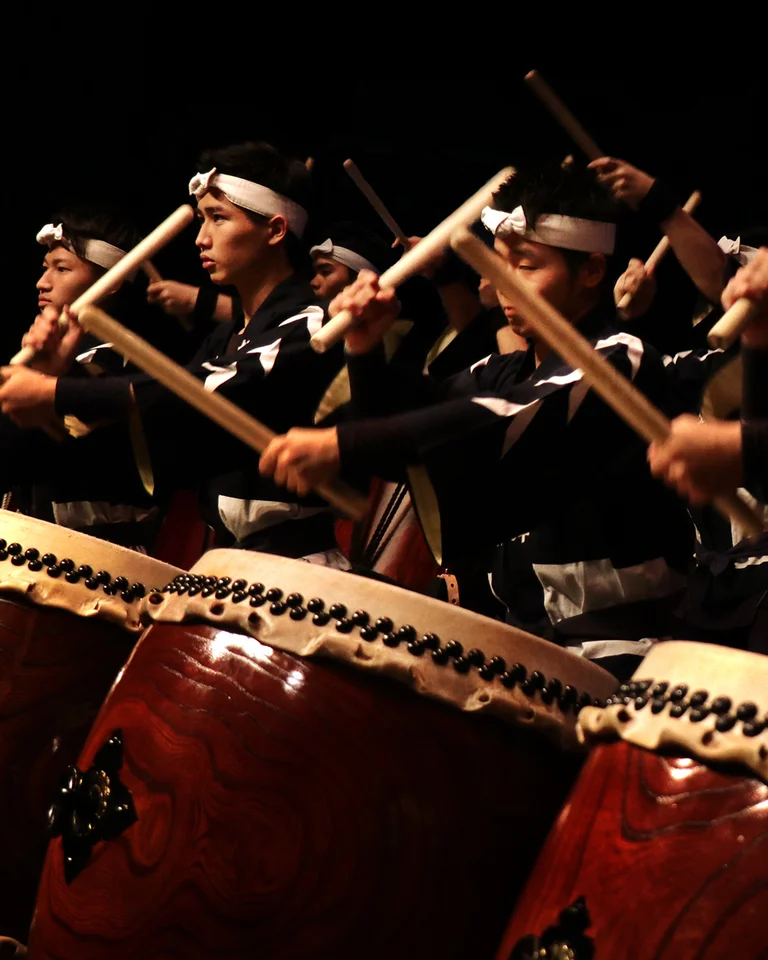 Group of Taiko drummers in traditional attire performing energetically on large drums during a captivating stage show.