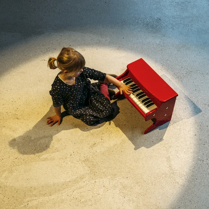 Junges Mädchen an einem roten Spielzeugklavier
