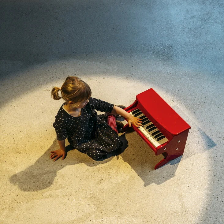 Junges Mädchen an einem roten Spielzeugklavier