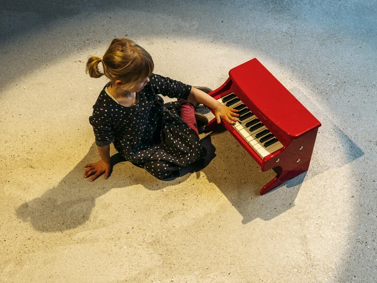 Junges Mädchen an einem roten Spielzeugklavier