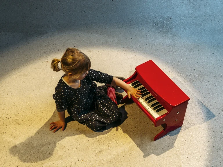 Junges Mädchen an einem roten Spielzeugklavier
