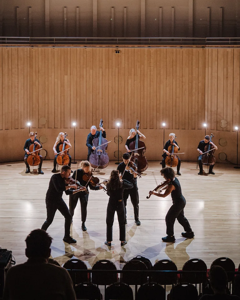 Eine Kammermusikgruppe (Scottish Ensemble ) spielt auf einer Bühne mit Streichinstrumenten. Die Musiker sind in einem halbkreisförmigen Arrangement aufgestellt.