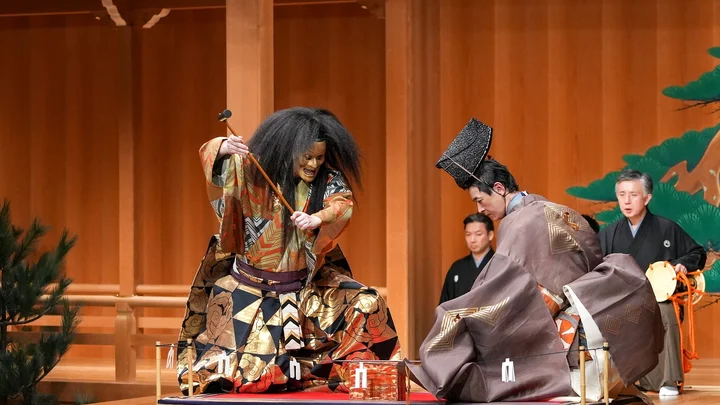 Zwei Künstler führen auf einer traditionellen Noh-Bühne auf. Einer trägt eine dekorative Maske, beide tragen prächtige Kimonos (Kokaji).