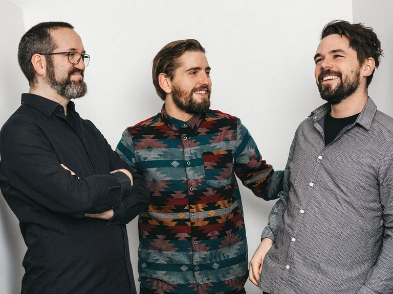 Drei Männer (Pablo Held Trio) stehen zusammen, lachen in entspannter Atmosphäre.