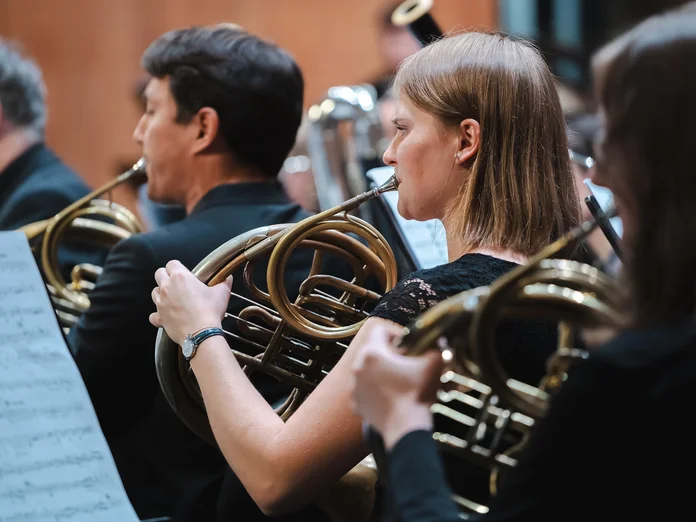 Musiker (Mahler Academy Orchestra) spielen Waldhörner in einem Orchester. Sie konzentrieren sich auf ihre Noten, während sie gemeinsam eine harmonische Melodie schaffen.