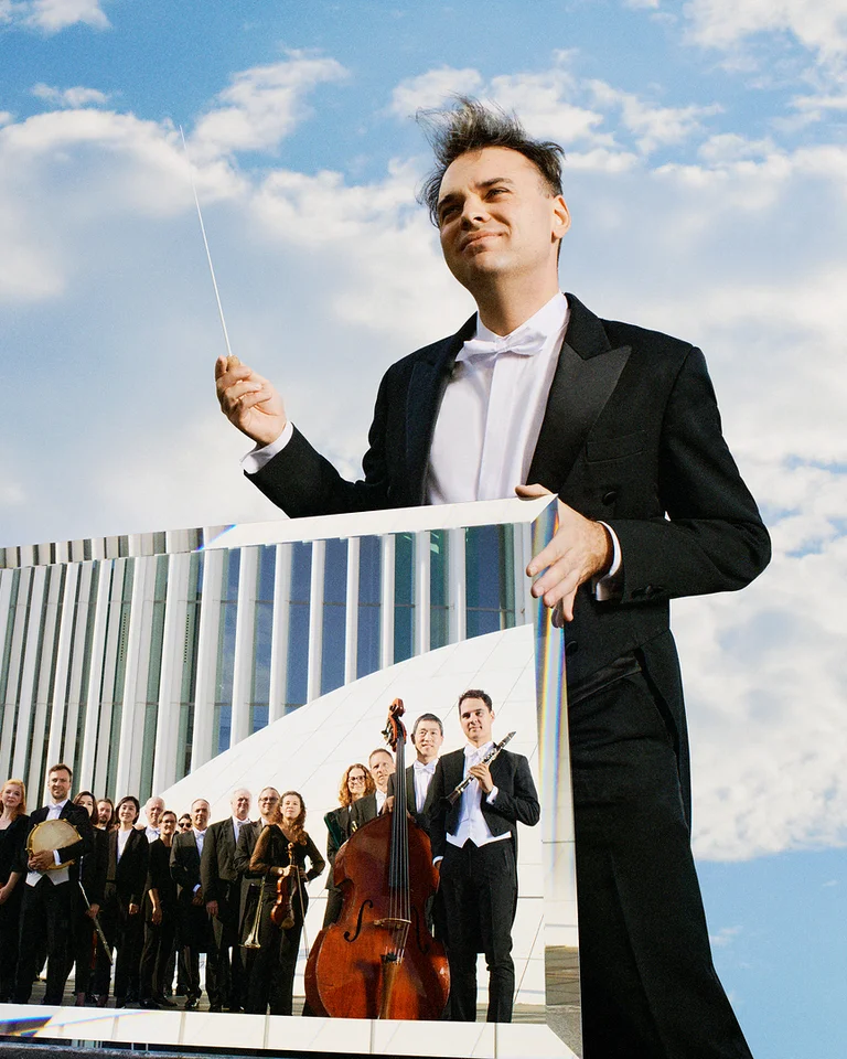 A conductor in a tuxedo holds a baton, reflecting an orchestra in a mirror, with a blue sky backdrop.