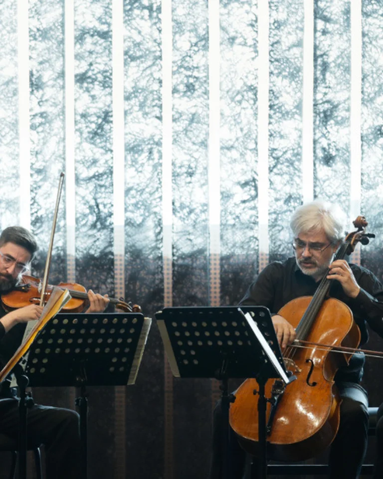 A string quartet with four musicians performs in front of an illuminated backdrop. Each musician is focused on their instrument.