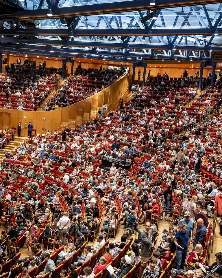 Kölner Philharmonie: Ein großes, voll besetztes Auditorium mit modernen Architekturelementen. Die Zuschauer sind zahlreich auf den roten Sitzen verteilt.