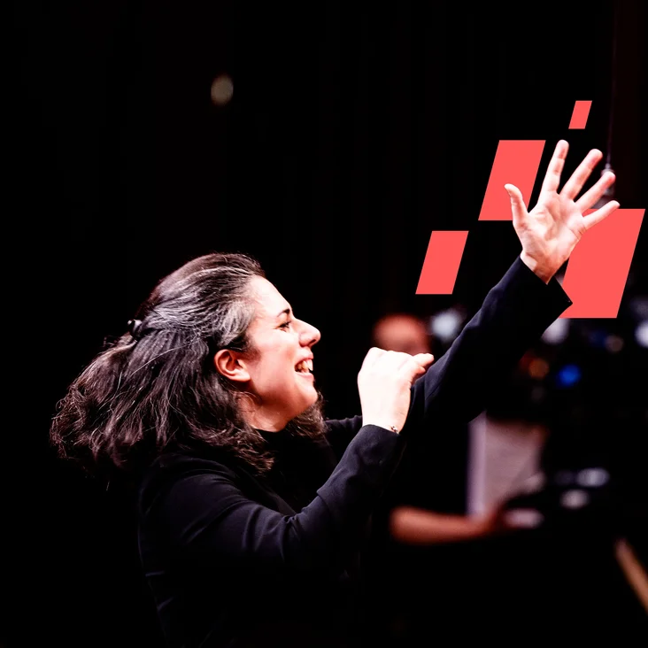 Eine Person dirigiert leidenschaftlich ein Orchester, mit erhobener Hand und dynamischem Gesichtsausdruck. Rote Rechtecke im Hintergrund.