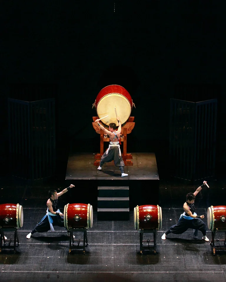 Sieben Trommler (Eitetsu Fu-un no Kai Taiko-Ensemble) auf der Bühne führen eine kraftvolle Taiko-Performance mit großen Trommeln auf, synchronisiert in traditioneller Kleidung.