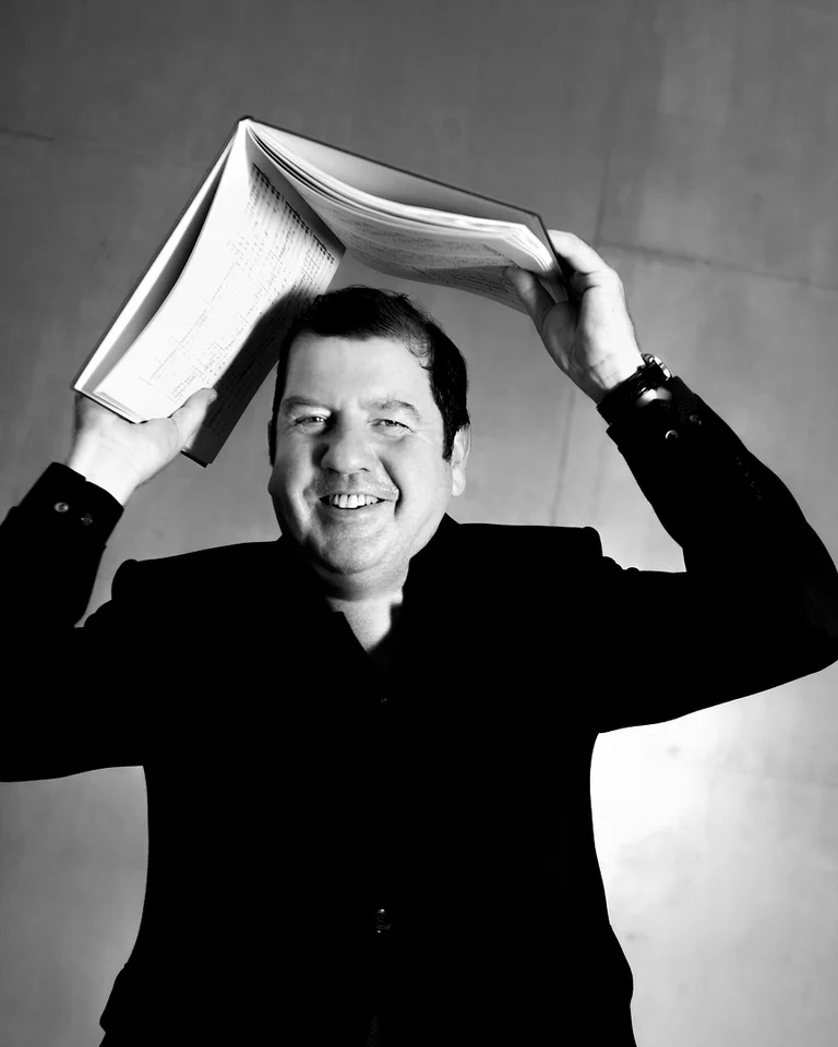 A smiling man holds a large open book over his head. Black-and-white photo with a simple background.