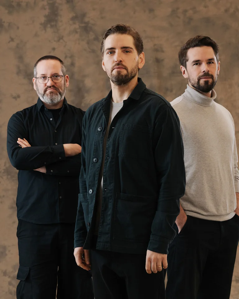 Drei Männer (Pablo Held Trio) stehen vor einem neutralen Hintergrund. Sie tragen lässige Kleidung und blicken ernst in die Kamera.