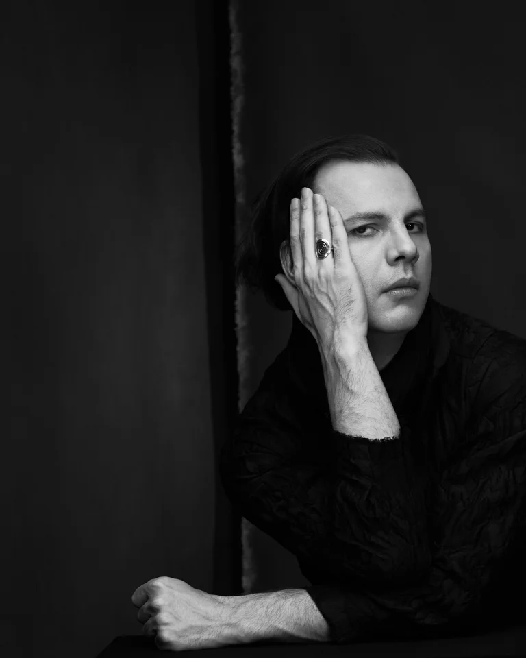 Schwarz-weiß Porträt einer Person, die mit der Hand das Gesicht stützt. Sie wirkt nachdenklich in einem dunklen Raum.