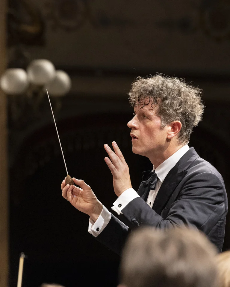 Der Dirigent Philipp von Steinaecker mit lockigem Haar und dunklem Anzug dirigiert ein Orchester.