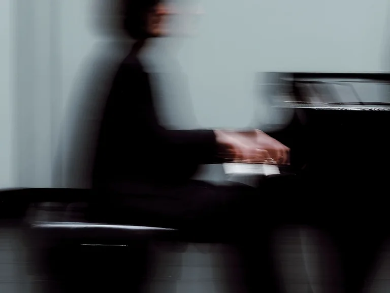 Ein unscharfer Musiker (Giorgi Gigashvili) spielt Klavier auf einer Bühne. Die verschwommene Bewegung vermittelt ein Gefühl von Dynamik und Geschwindigkeit.