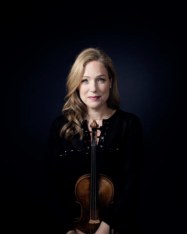 Eine Frau (Isabelle van Keulen) in schwarzer Kleidung hält eine Geige. Dunkler Hintergrund hebt ihre Erscheinung und das Instrument hervor.