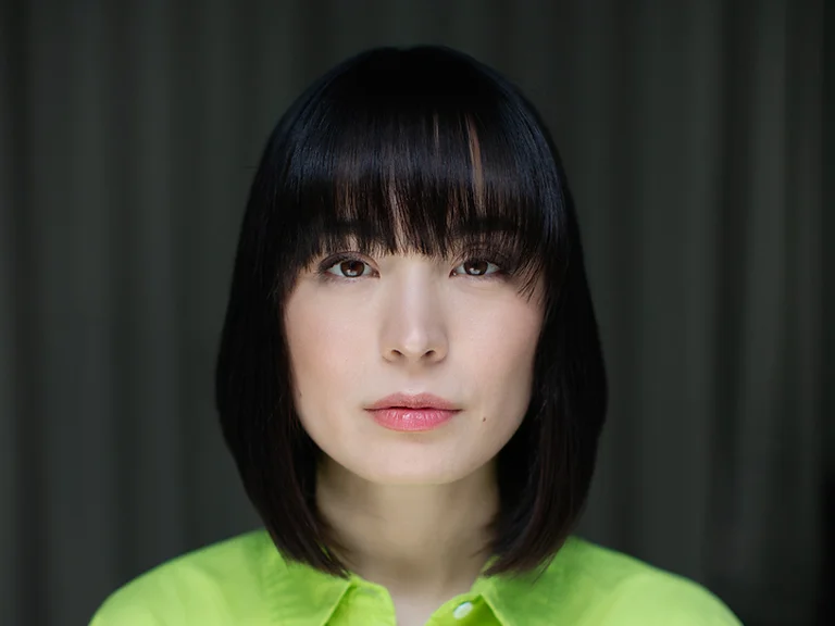 Eine Frau (Alice Sara Ott) mit glattem, dunklem Haar und einem Pony, trägt ein leuchtend grünes Hemd. Der Hintergrund ist dunkel gehalten.
