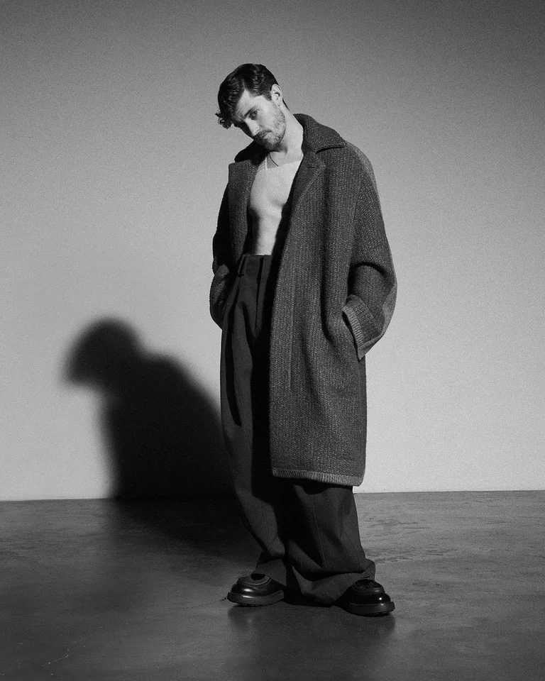 Schwarz-Weiß-Foto eines Mannes (Jakub Józef Orliński) in einem offenen Mantel, der lässig posiert. Sein Schatten ist deutlich auf dem Boden zu sehen.