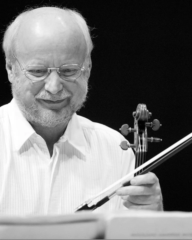 Ein älterer Mann (Günter Pichler) spielt eine Violine und lächelt. Er trägt ein weißes Hemd und konzentriert sich auf die Musik.