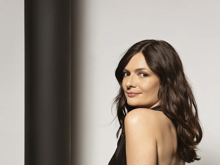 Marianne Crebassa mit langen, dunklen Haaren in schulterfreiem Top und hellhose blickt über die Schulter.