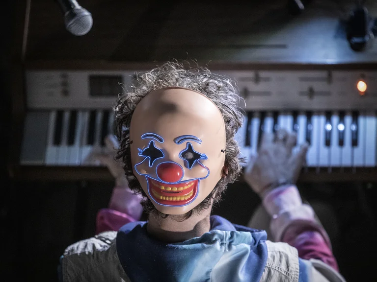 Ein Mensch trägt eine Clownsmaske und spielt auf einem Keyboard. Eine Mikrofonaufnahme von oben ist sichtbar.