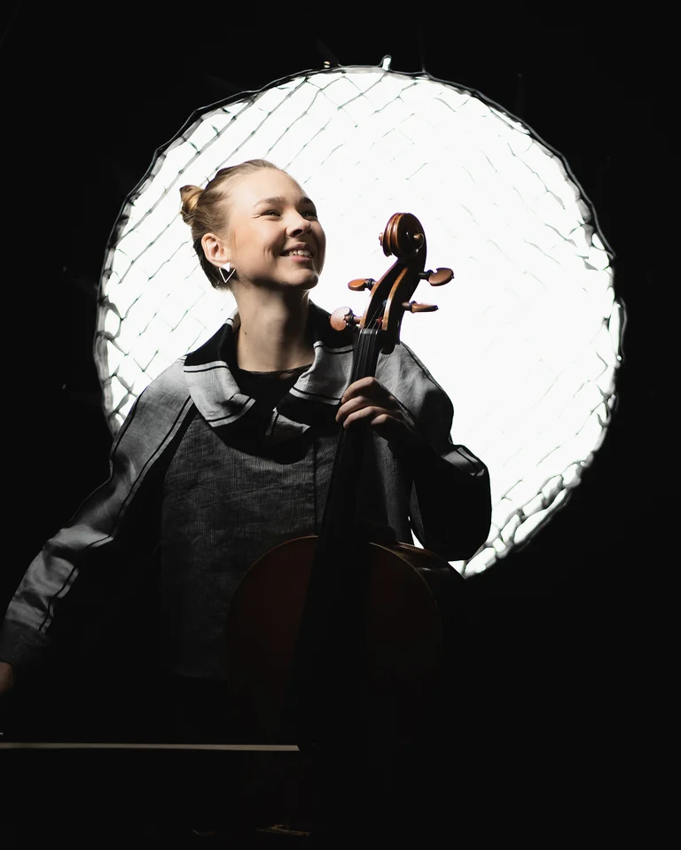 Valerie Fritz posiert mit ihrem Cello vor einer Studiobeleuchtung, umgeben von Dunkelheit.