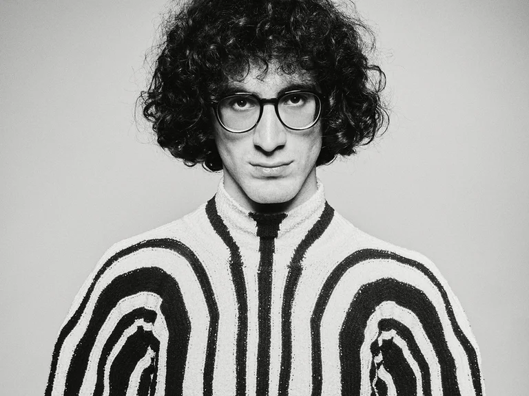 Schwarzweiß-Foto einem Mann (Giorgi Gigashvili) mit lockigem Haar und Brille, die einen gestreiften Pullover trägt. Ausdruck ist ernst.